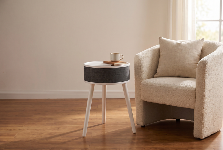 White round side table space heater with a charcoal fabric drum beside a cream armchair