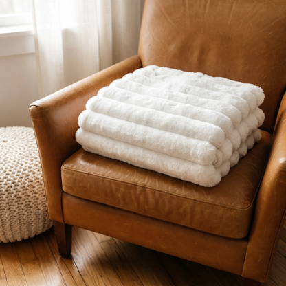 White ruched faux fur throw folded on a caramel leather armchair