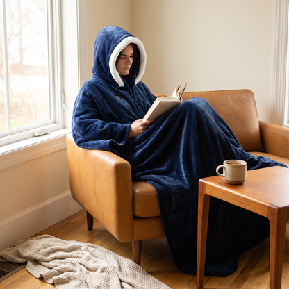 Woman reading in an armchair wearing the dark blue hooded flannel wearable blanket