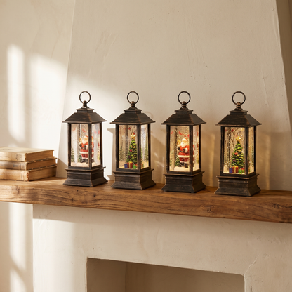 Four small bronze LED lanterns, two Santa and two Christmas tree, on a wood mantel