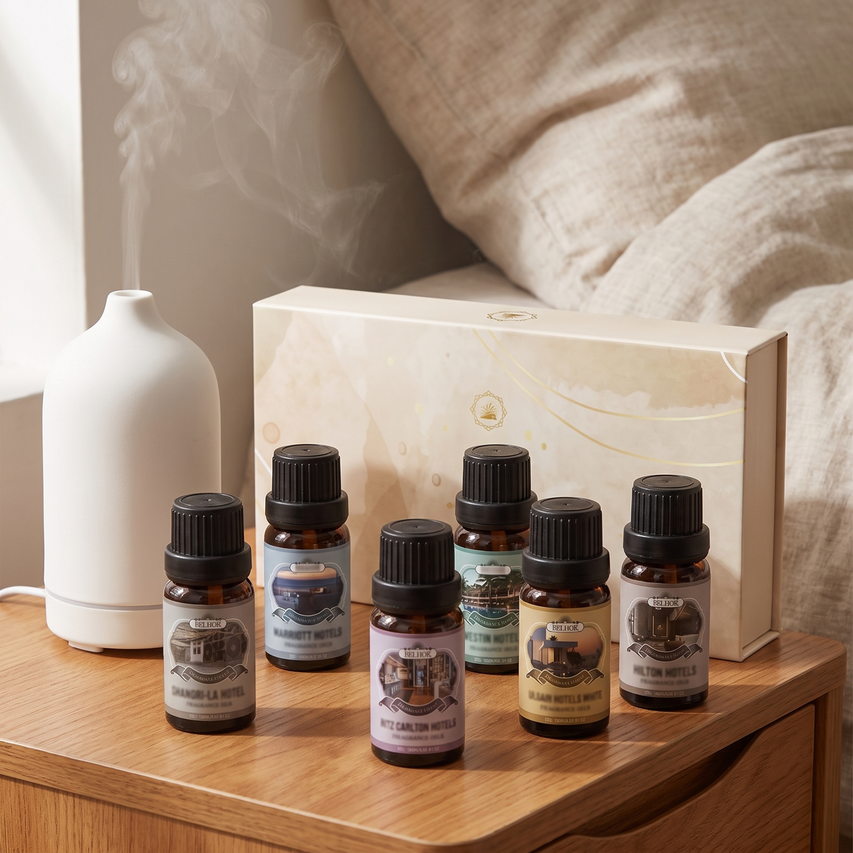 Fragrance oil set and cream gift box beside a white ceramic diffuser on a bedroom nightstand